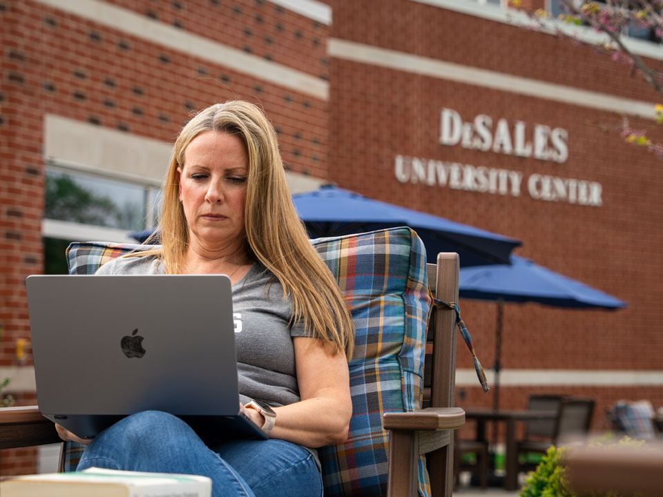 female student working on laptop outside of campus building