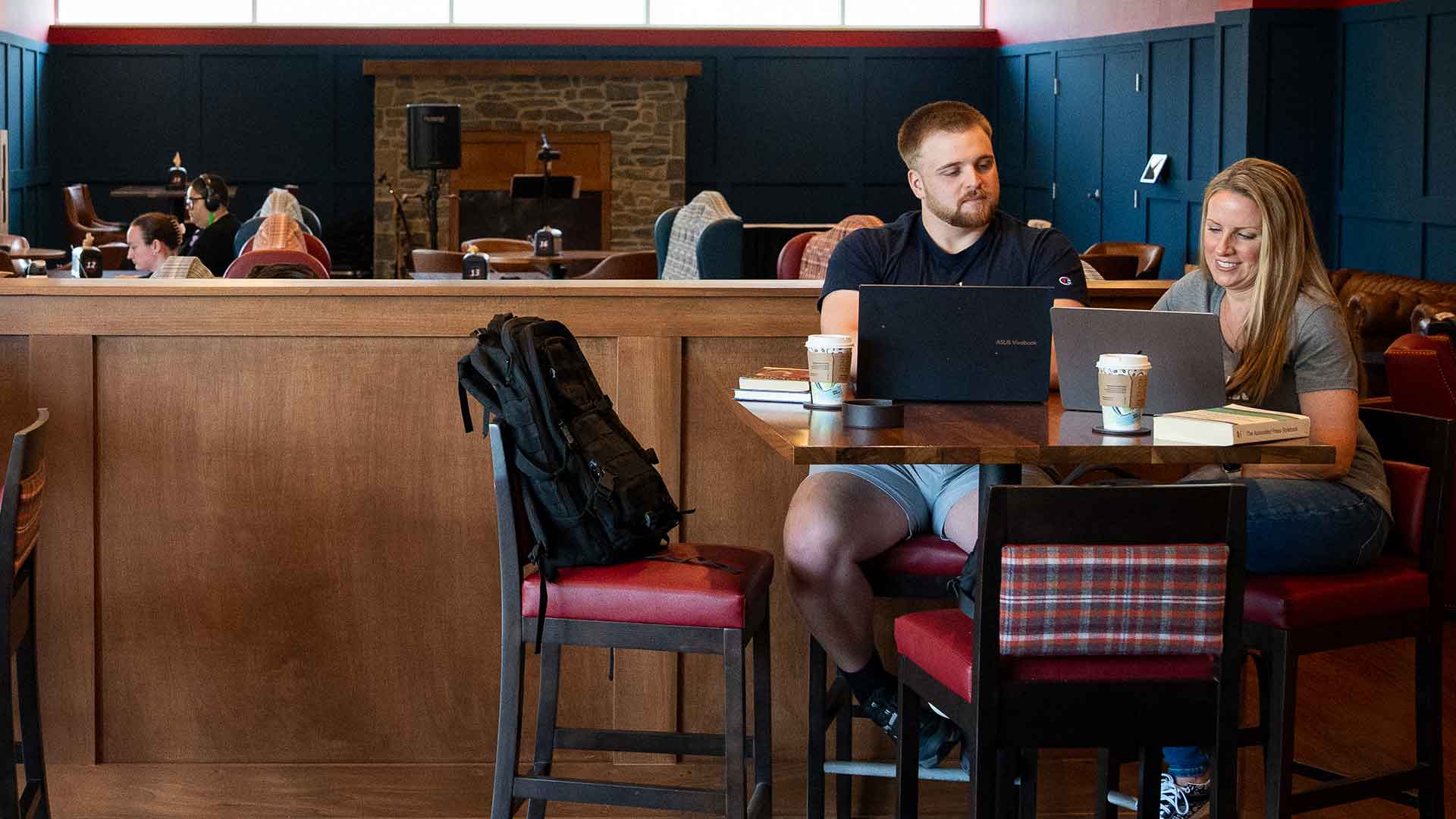 two adult students working on laptops in a cafe